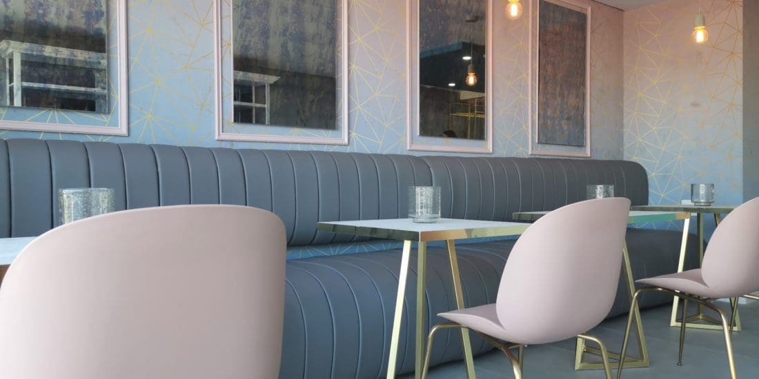 retail design built in booth seat with pleated vinyl fabric, smoked glass mirrors with pink frames, geometric wallpaper design, gold details